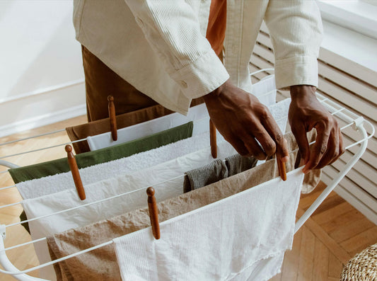 Hands pinning clean laundry with wooden clothespins onto a white folding drying rack indoors