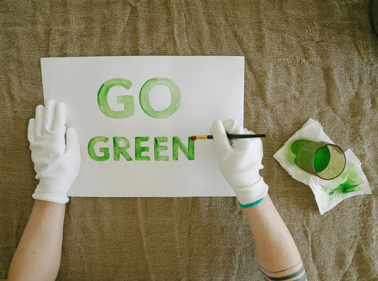 Gloved hands painting the words Go Green in green watercolor on white paper