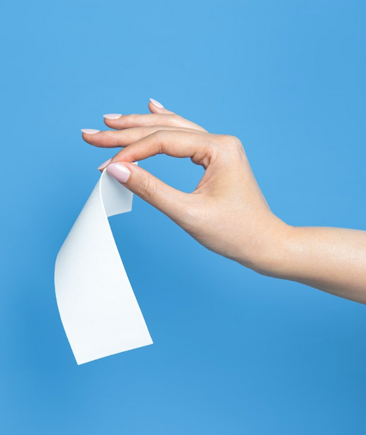 Hand holding a single white laundry detergent sheet against a blue background