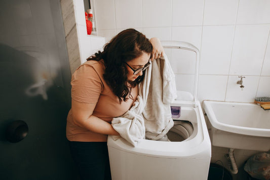 Woman loading a washing machine with laundry indoors. Domestic life in modern laundry room.