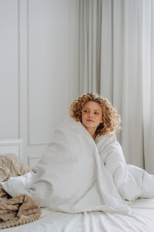 Caucasian woman enjoying a cozy morning wrapped in a blanket on a comfortable bed.