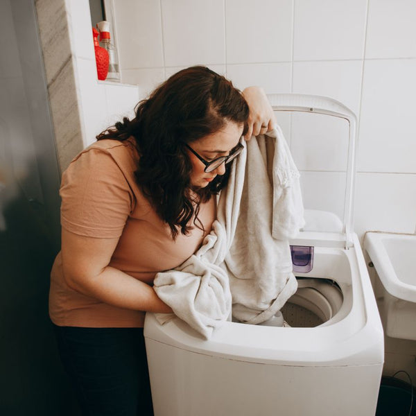 Woman loading a washing machine with laundry indoors. Domestic life in modern laundry room.
