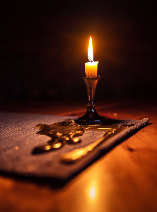 Close-up of a candle casting warm light in a dark setting, creating a cozy ambiance.