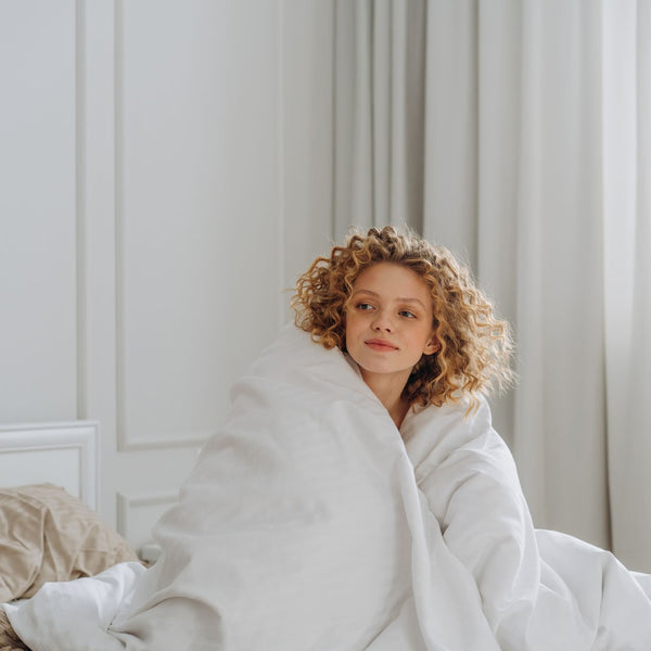 Caucasian woman enjoying a cozy morning wrapped in a blanket on a comfortable bed.