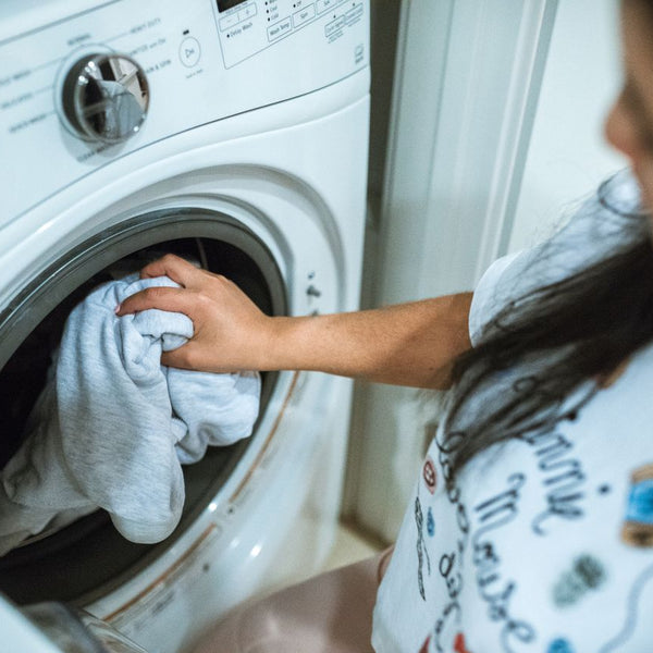 A woman loading laundry into a washing machine indoors, focusing on household chores.