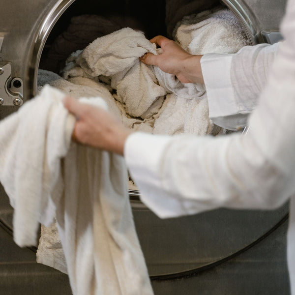 A person loading towels into an industrial washing machine in a launderette.