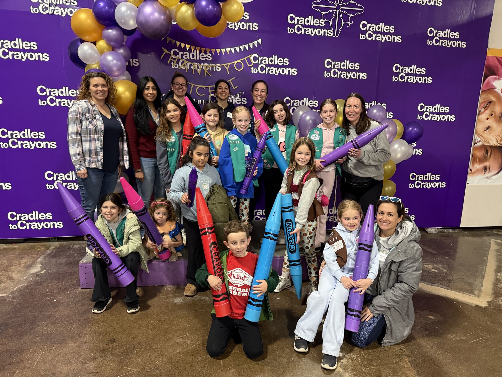 Volunteers and kids holding giant crayons at Cradles to Crayons